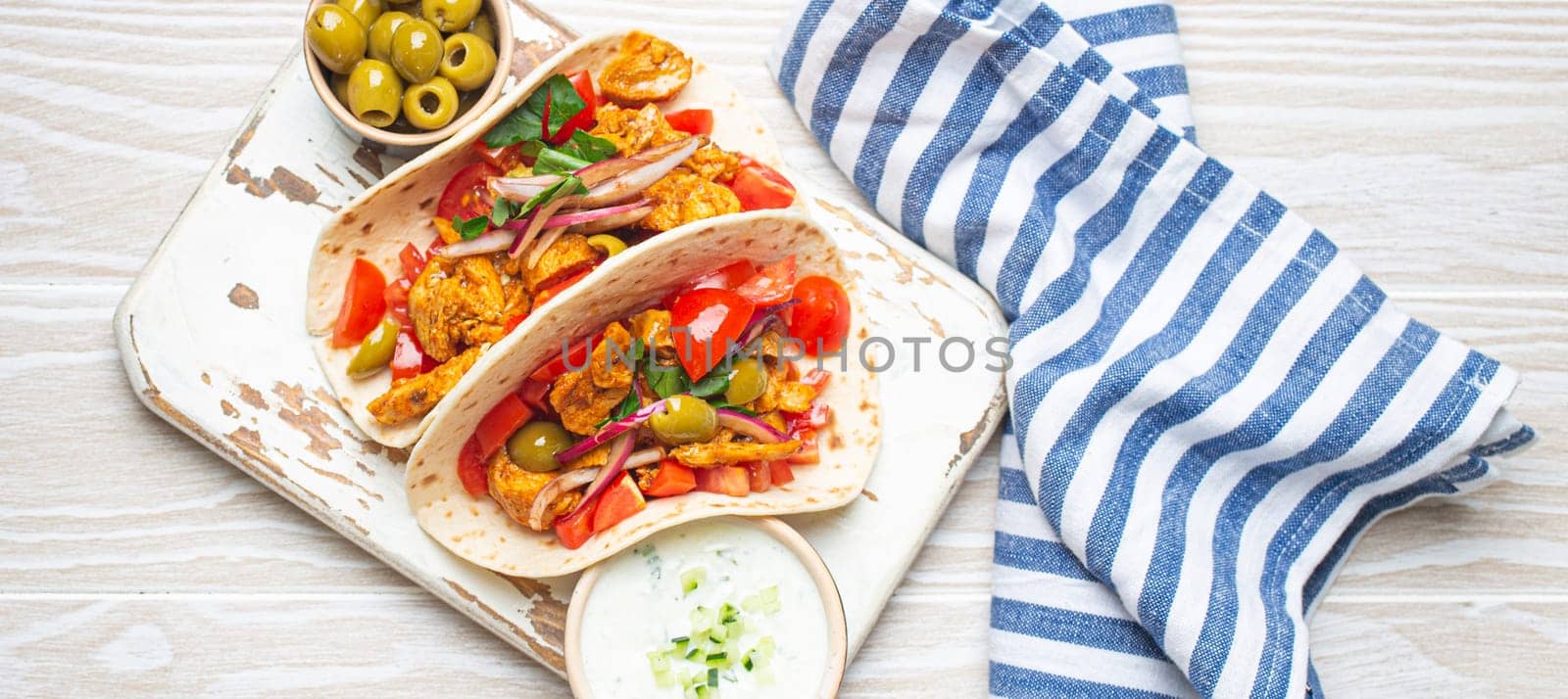Traditional Greek Dish Gyros: Pita bread Wraps with vegetables, meat, herbs, olives on rustic wooden cutting board with Tzatziki sauce, olive oil top view on white wooden summer background. by its_al_dente