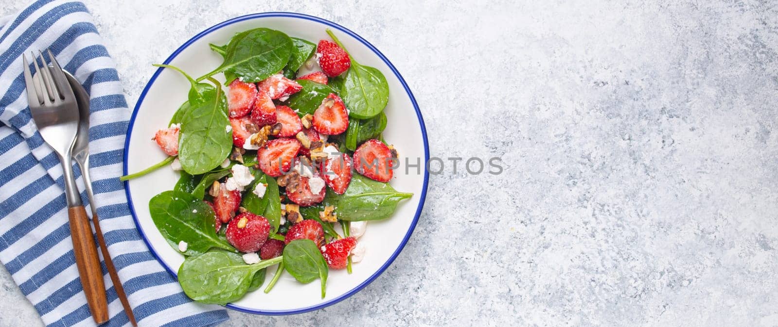 Light Healthy Summer Salad with fresh Strawberries, Spinach, Cream Cheese and Walnuts on White Ceramic Plate, white rustic stone Background From Above, Space For Text.