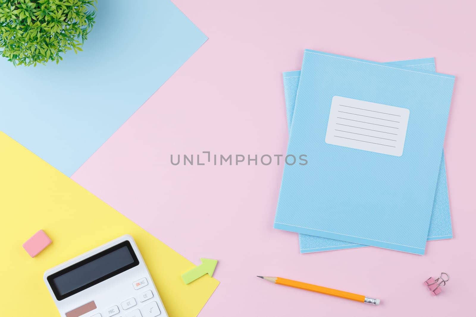 Notebooks with colored paper and calculator on a pink background. Back to school concept. Flat lay. Pencil with an elastic band on the school desk. Top view.