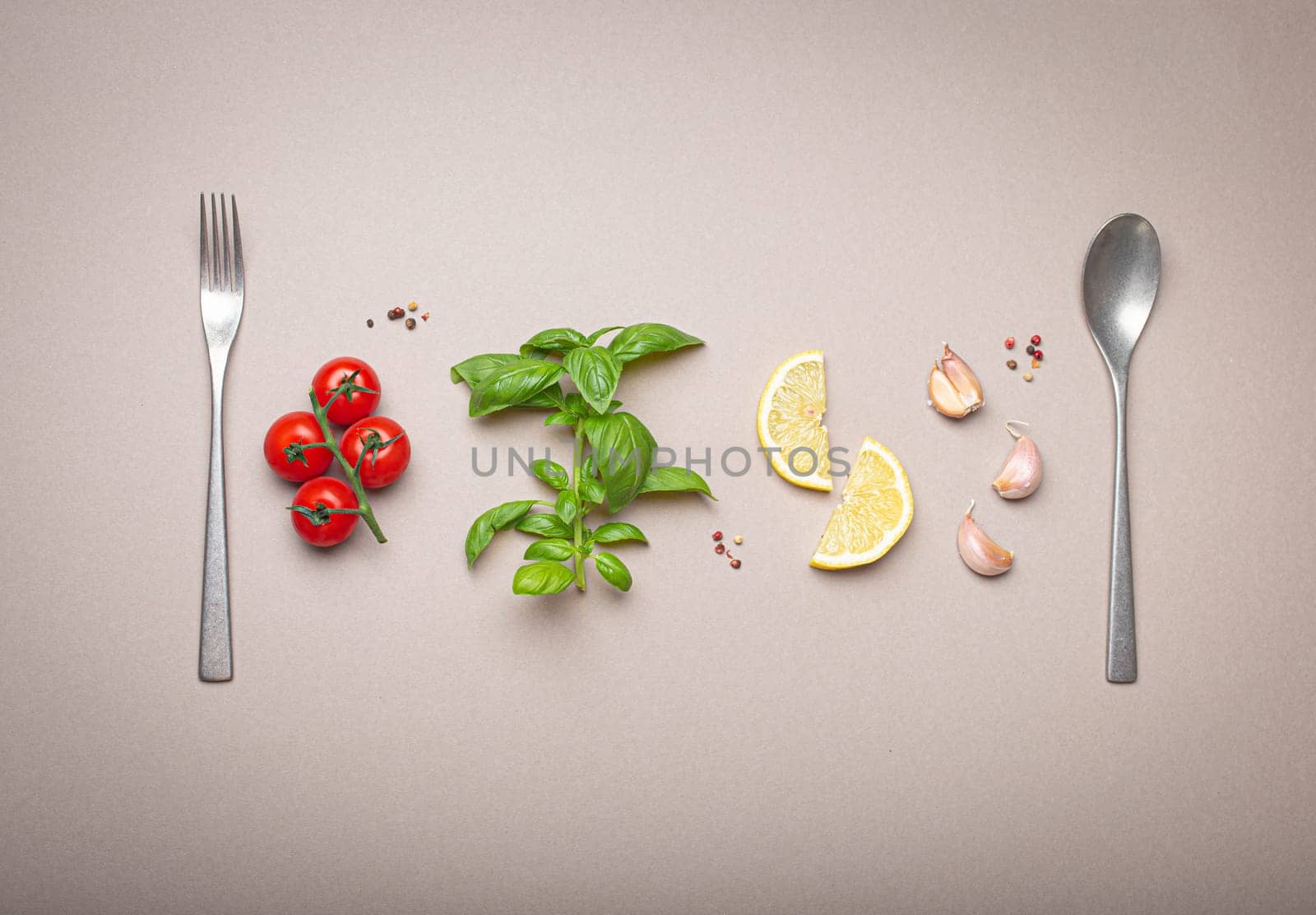 Composition with branch of fresh cherry tomatoes, basil branch, garlic cloves, lemon wedges, kitchen spoon and fork on minimalistic grey clean background, overhead shot by its_al_dente