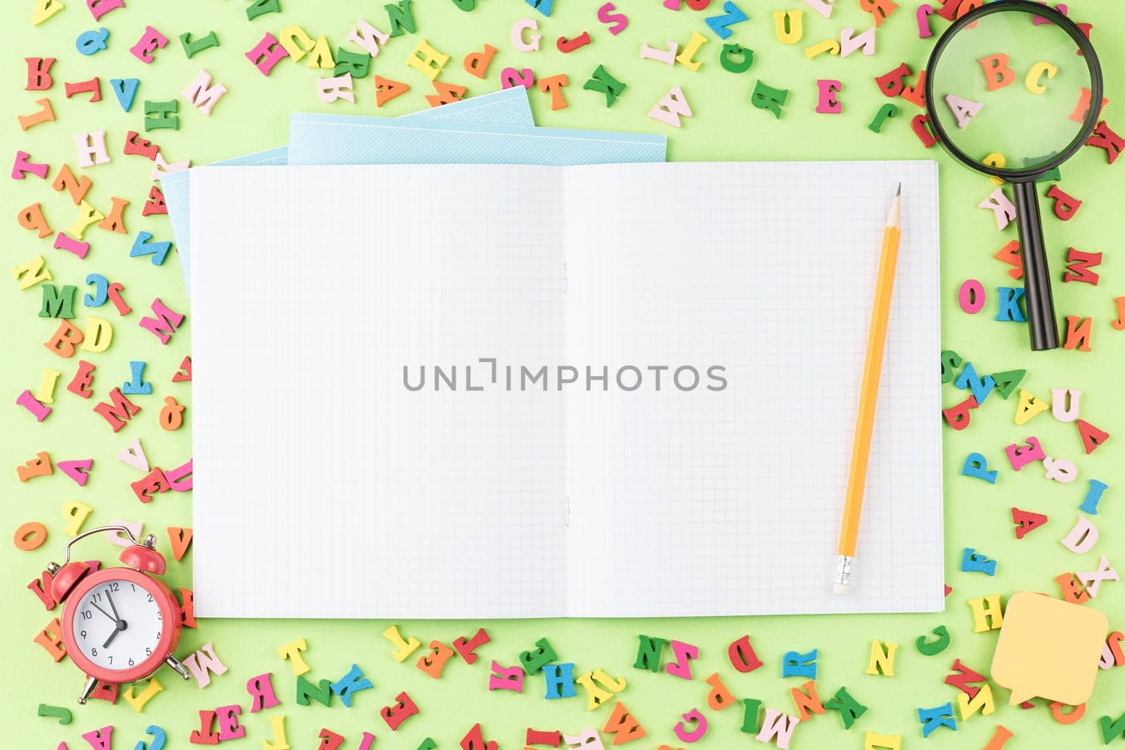 Open spiral notebook on a green background with multicolored wooden letters. Top view. Back to school concept. Scattered alphabet on the school desk. Flat lay.