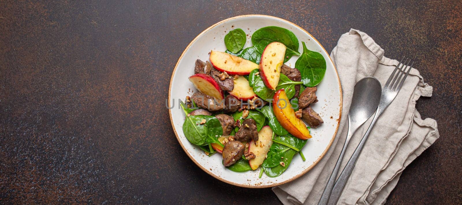 Healthy Salad with Iron Rich Ingredients Chicken Liver, Apples, Fresh Spinach and Walnuts on White Ceramic Plate, Dark Brown Rustic Stone Background Top View Copy Space.