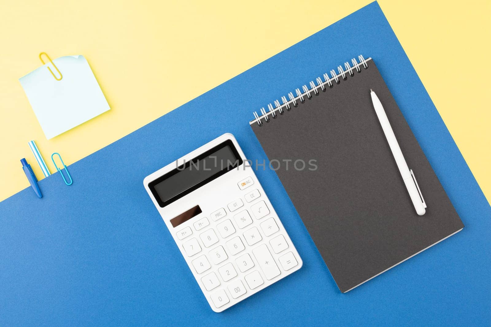 Spiral open notebook with pen and calculator on two tone background. School table concept. Office workplace. Top view, flat lay.