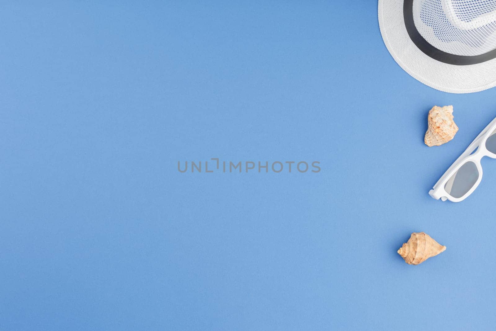 Beach hat with sunglasses on blue isolated background with copy space. Flat lay. Summer vacation concept. Seashells top view.