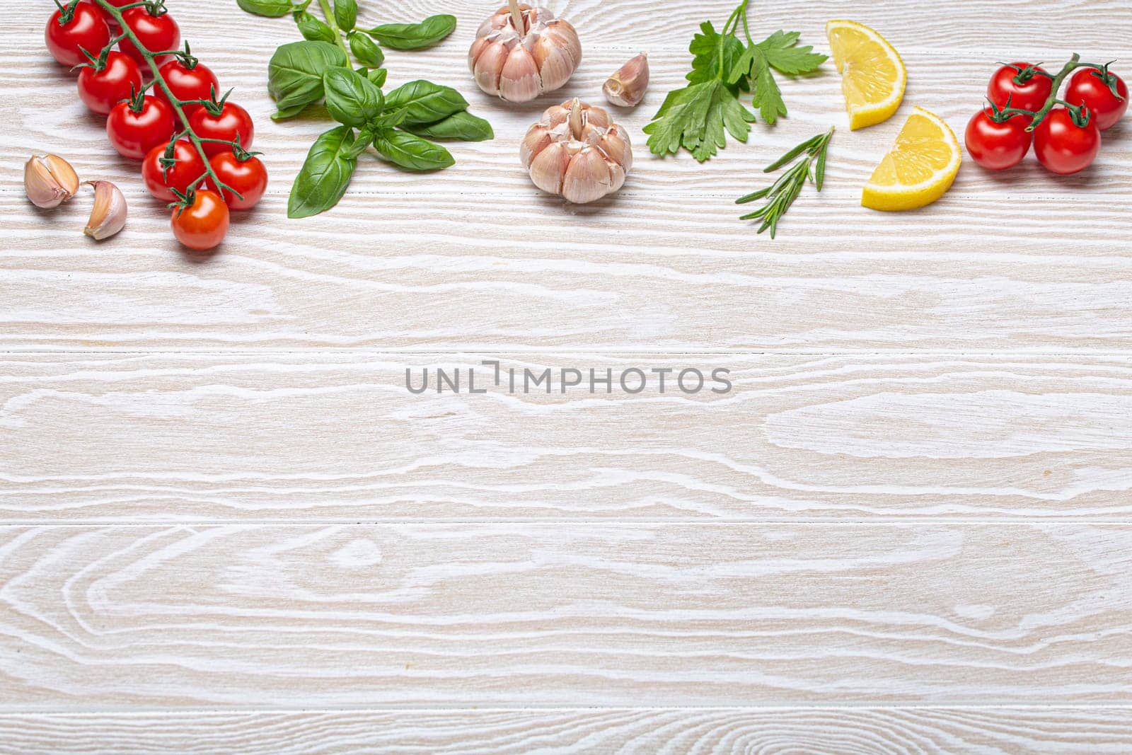 Healthy food ingredients composition with fresh cherry tomatoes, herbs, garlic cloves, lemon wedges on white wooden shabby background, overhead shot with copy space by its_al_dente