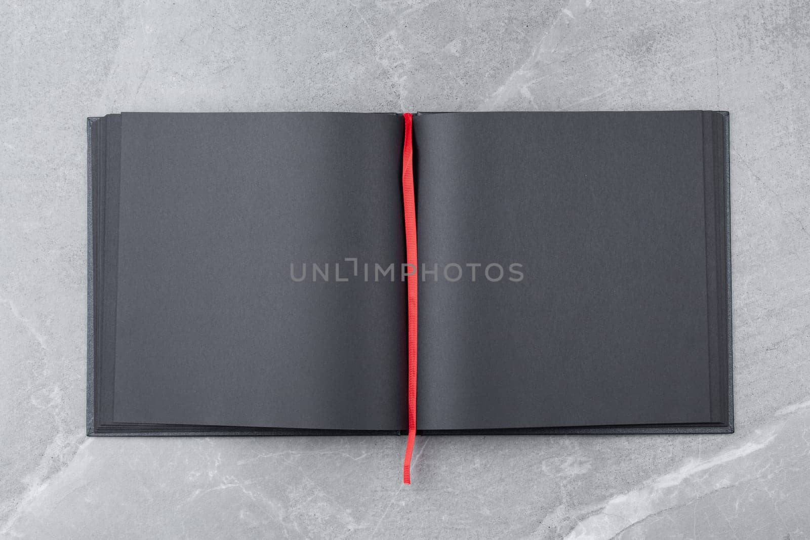 Open black notebook with blank pages and red bookmark on gray marble background. Top view.