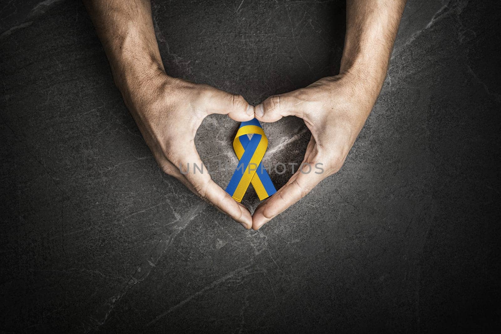 male hands with yellow and blue ribbon on marble background. concept needs help and support, truth will win