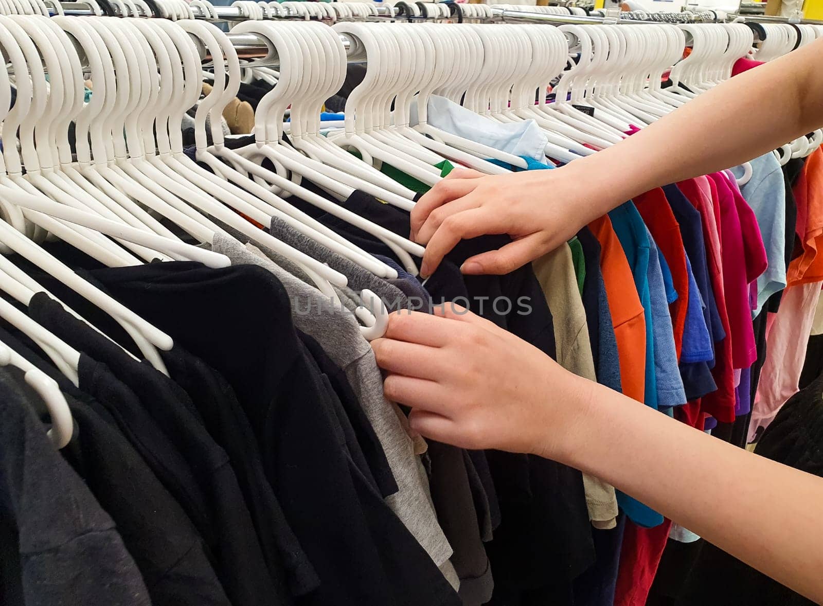 Women's hands are sorting through clothes on hangers. Second-hand. Old clothes are hung on hangers in the store.