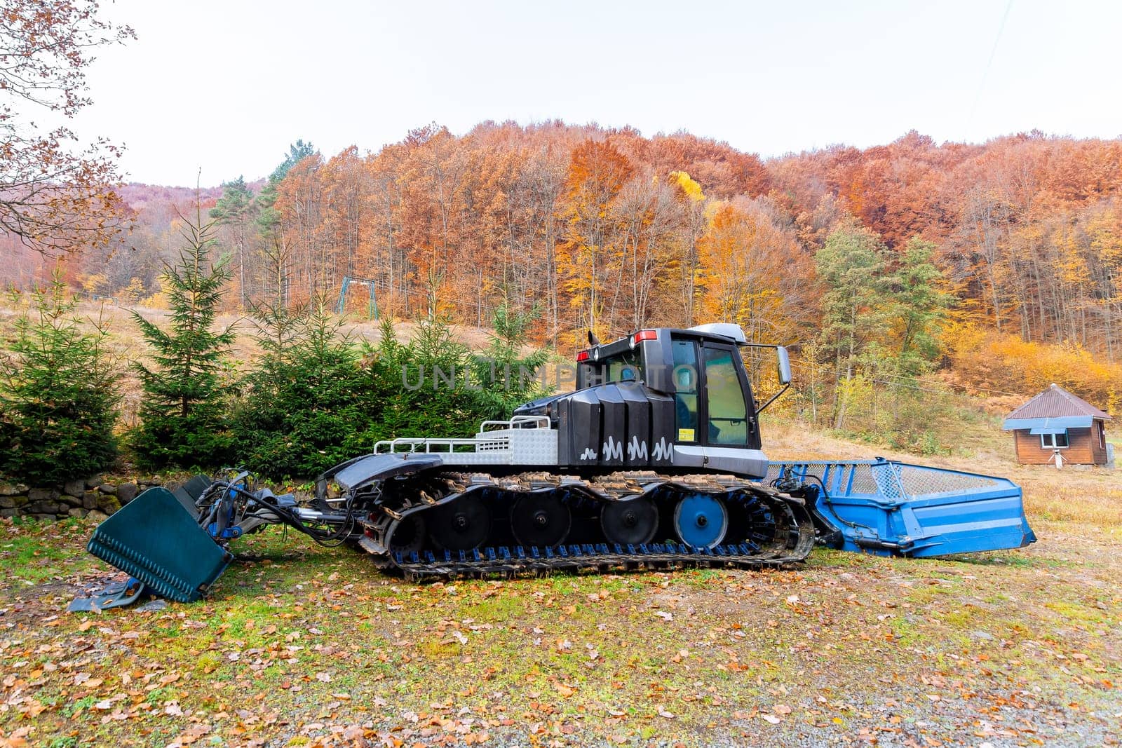 Crawler tractor is standing near the forest in the autumn season. Equipment for collecting snow in mountainous terrain.