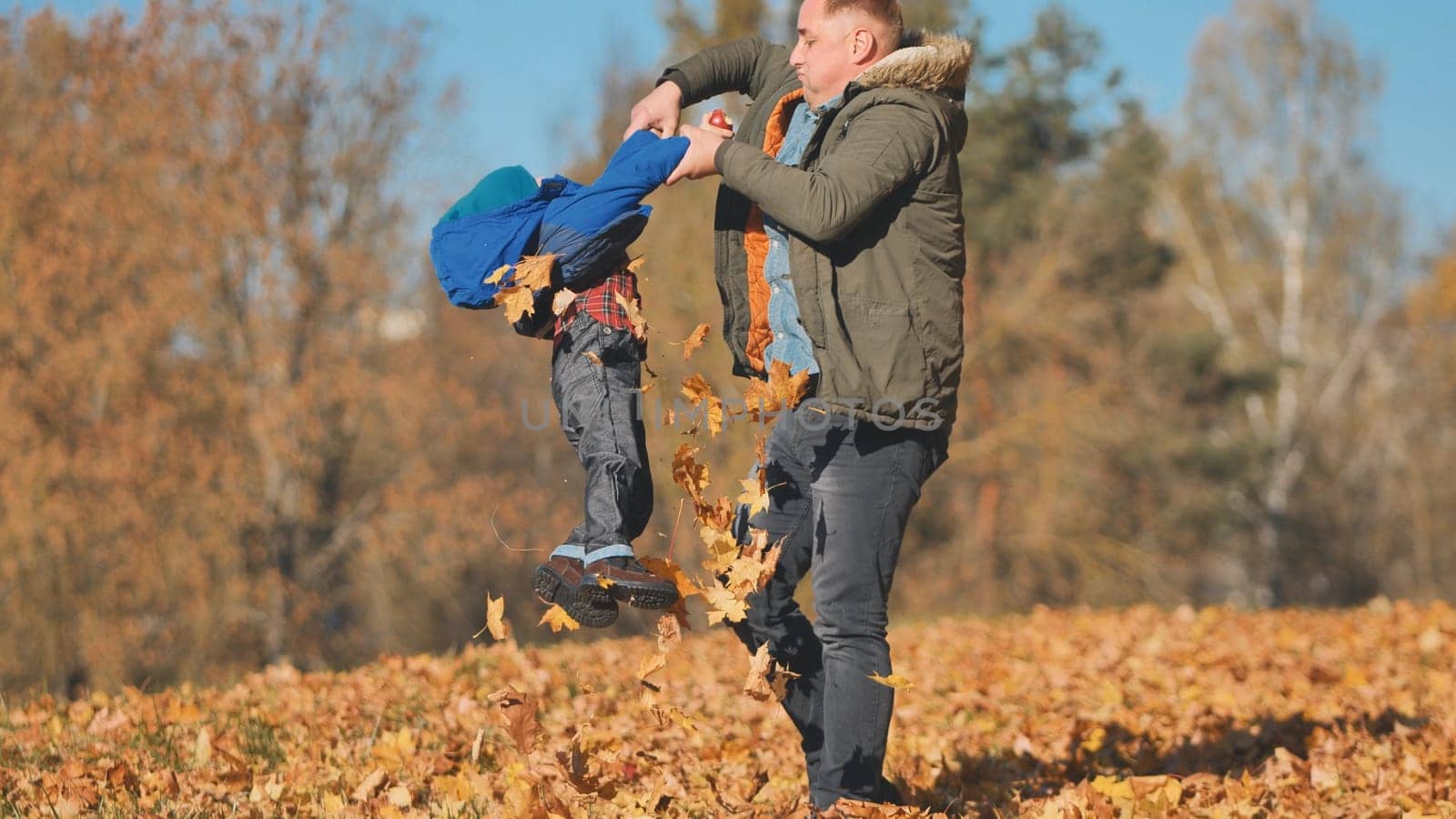 A father spins his son by his feet in the park in the fall