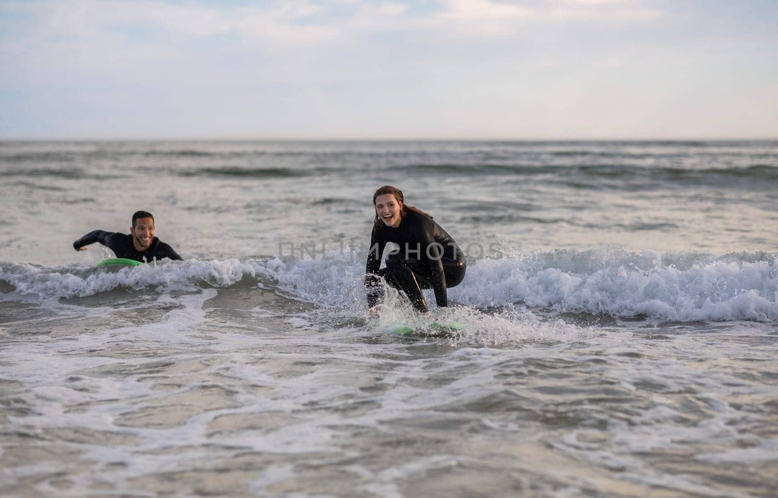 Cheerful Young Surfers Couple Surfing Together On The Beach In Summer, Happy Millennial Man And Woman Riding Waves On Surfboards, Laughing And Having Fun, Enjoying Water Sports, Copy Space