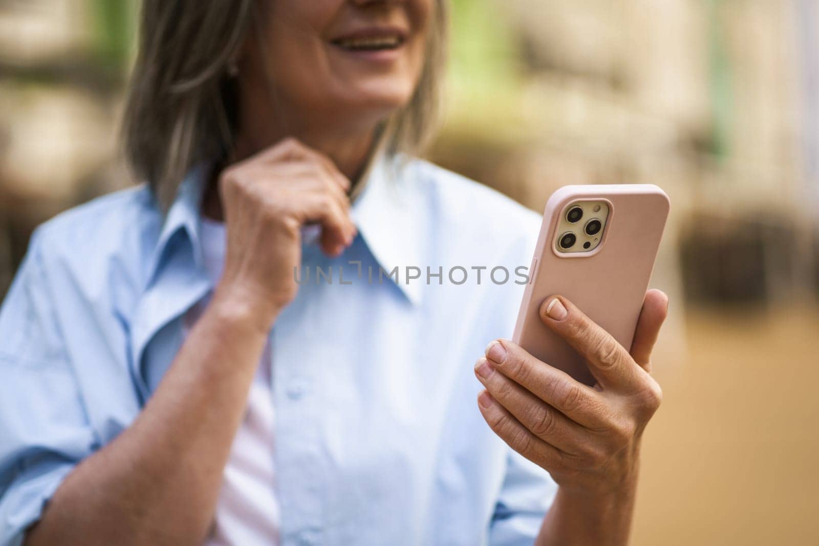 hands of a senior woman holding a mobile phone, emphasizing the concept of communication in old age. The image showcases the woman's fingers as she texts a message on the phone, highlighting her engagement with modern technology. by LipikStockMedia