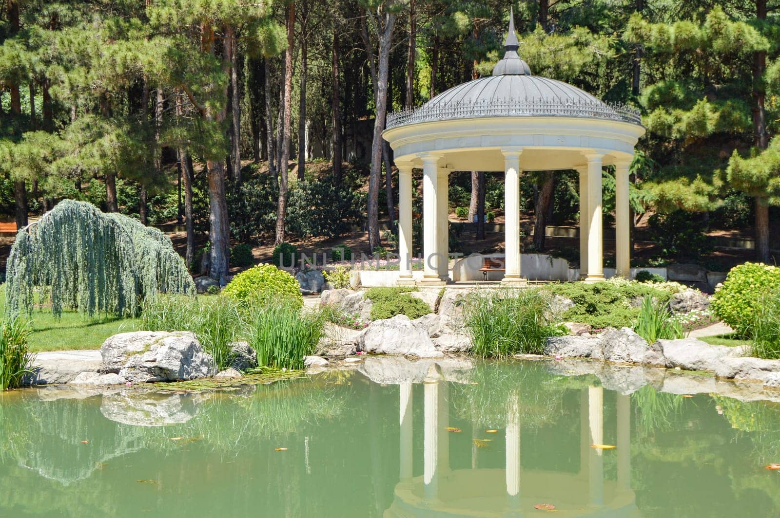 Picturesque view of the round gazebo by the fish pond, sunny summer day.