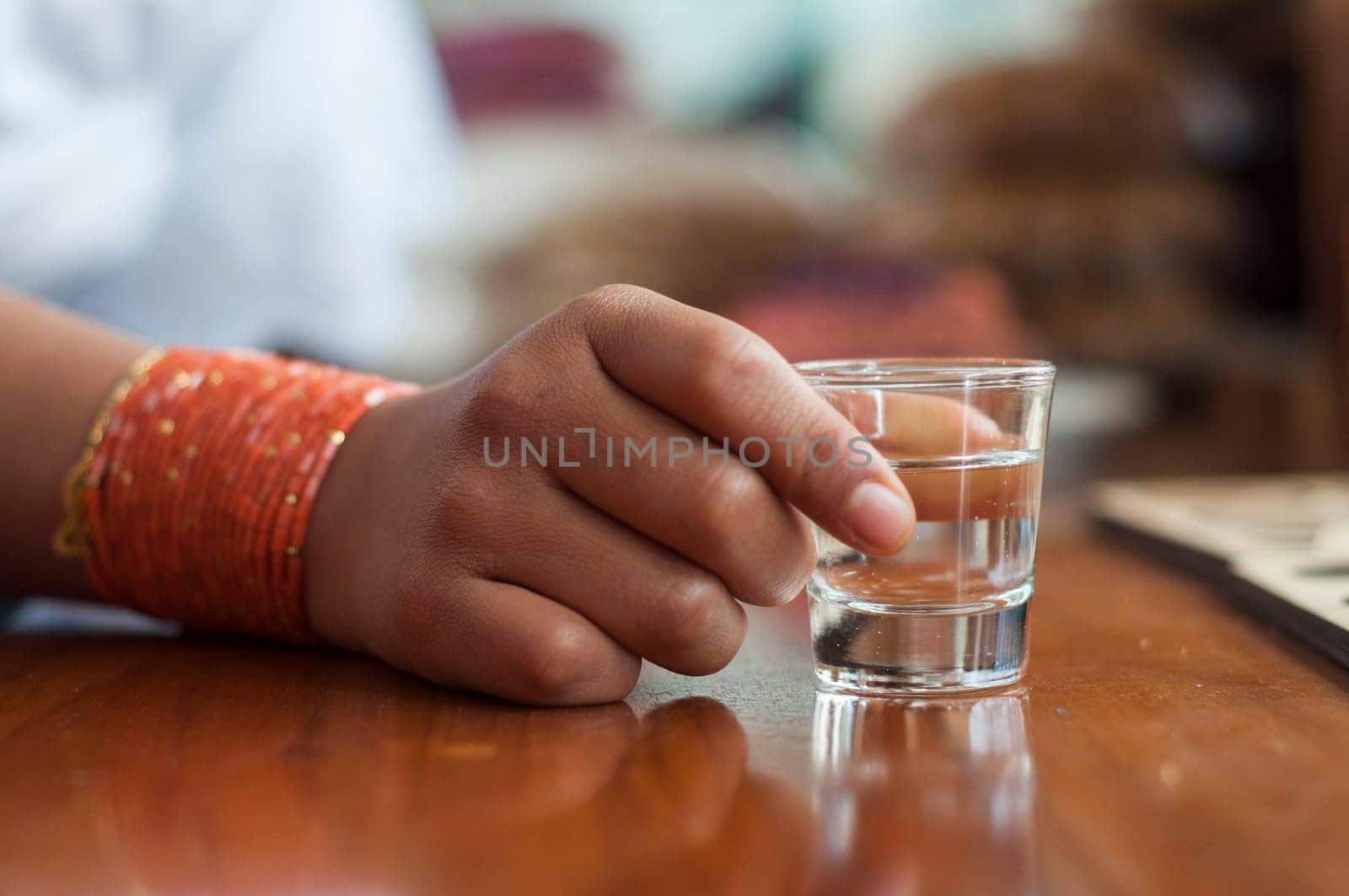 closeup of an indian girl hand holding a shot of alcohol on a wooden table. High quality photo