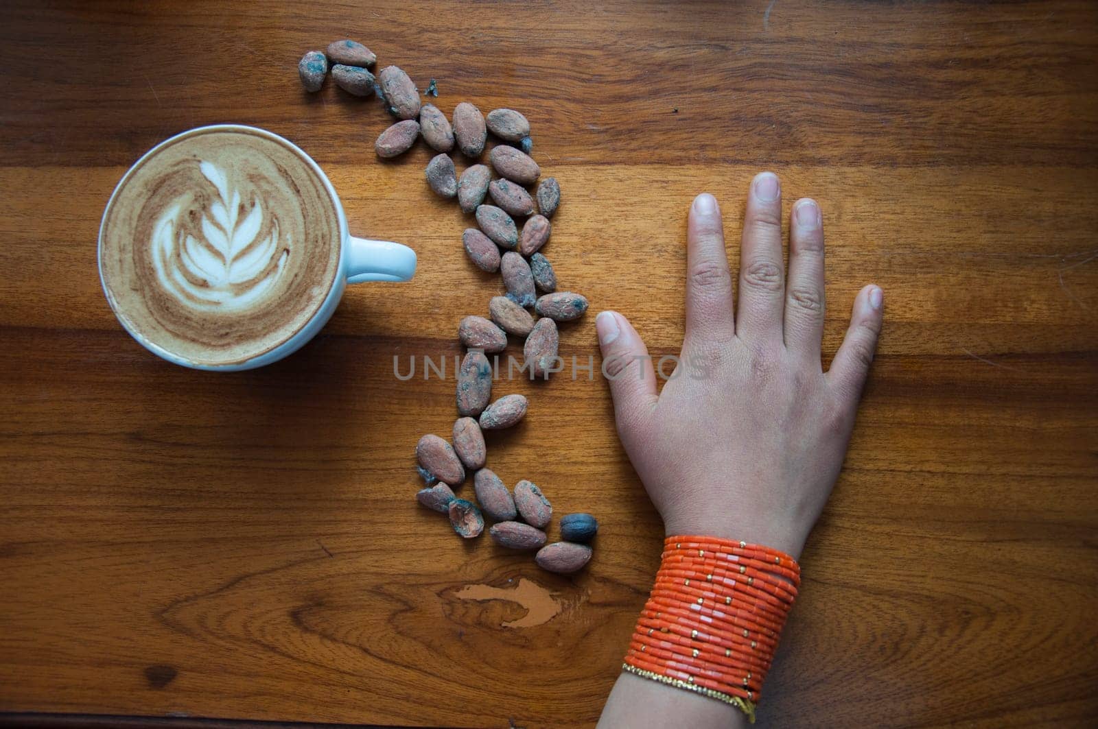 composition of a cup of coffee a hand of an indigenous girl and some coffee beans in the shape of an s. High quality photo