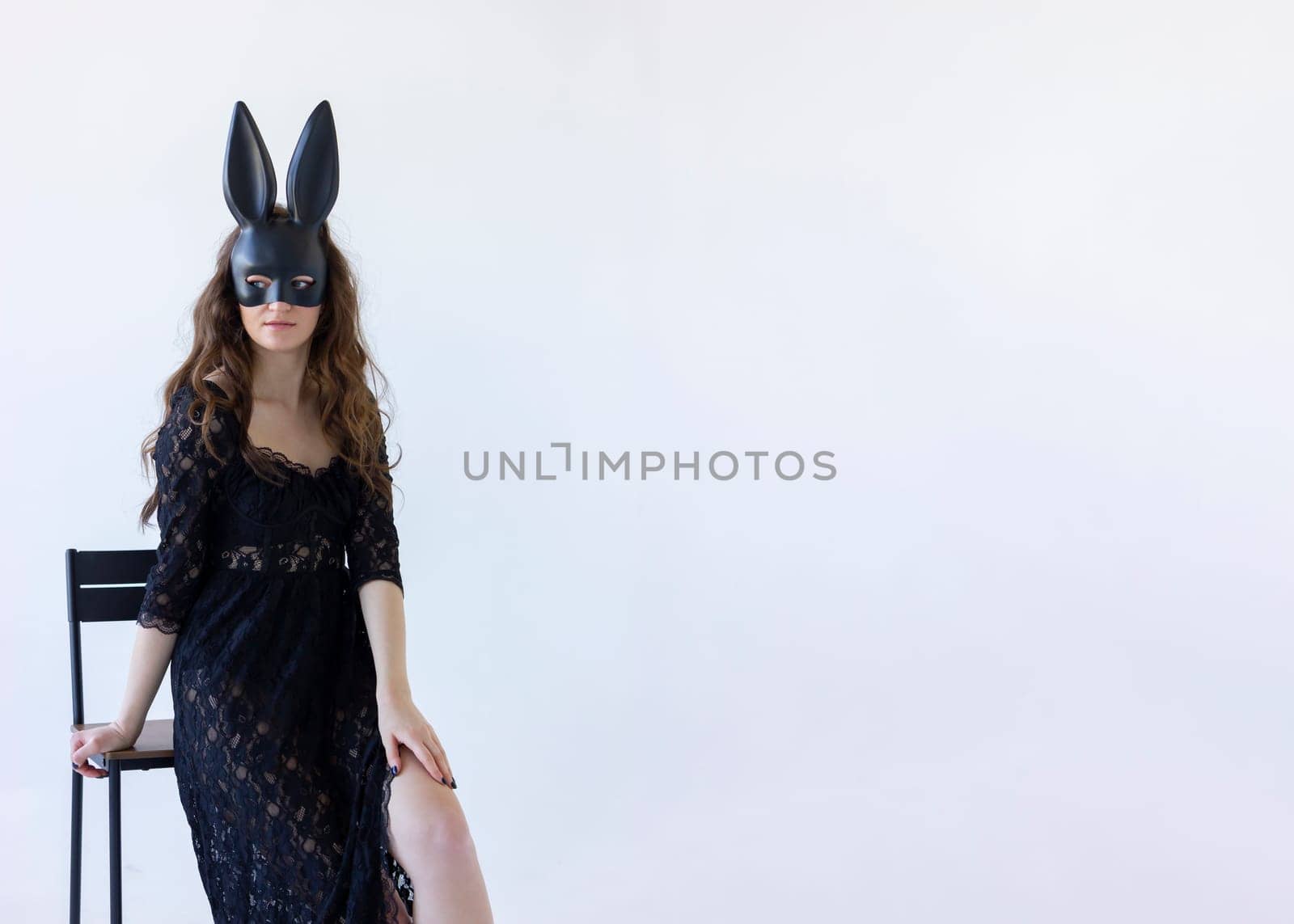 Mockup Young Woman Wearing Rabbit Black Mask On Face Sitting on chair white background, Pretty Bunny Girl with Long Ears Posing On Isolated Wall. Copy Space For Text, Horizontal lane.