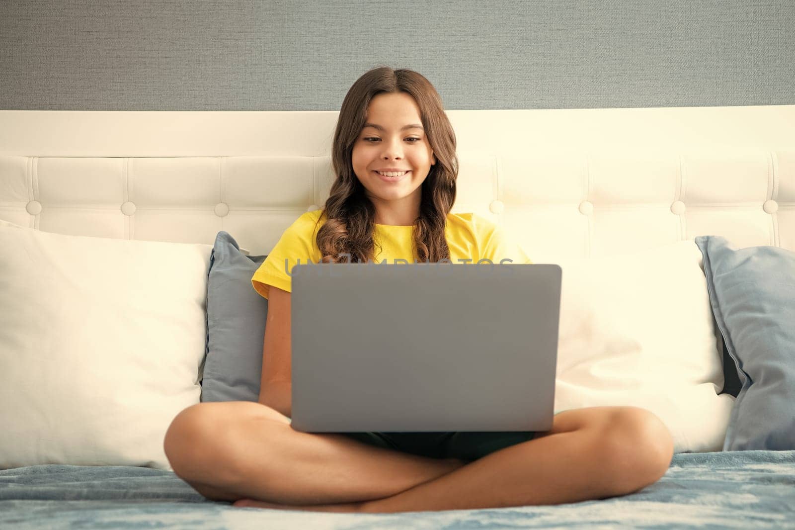 Young teenage girl, little student studying virtual course, learning distance class taking web training, looking at laptop computer watching online video lesson on bed at home. by RedFoxStudio