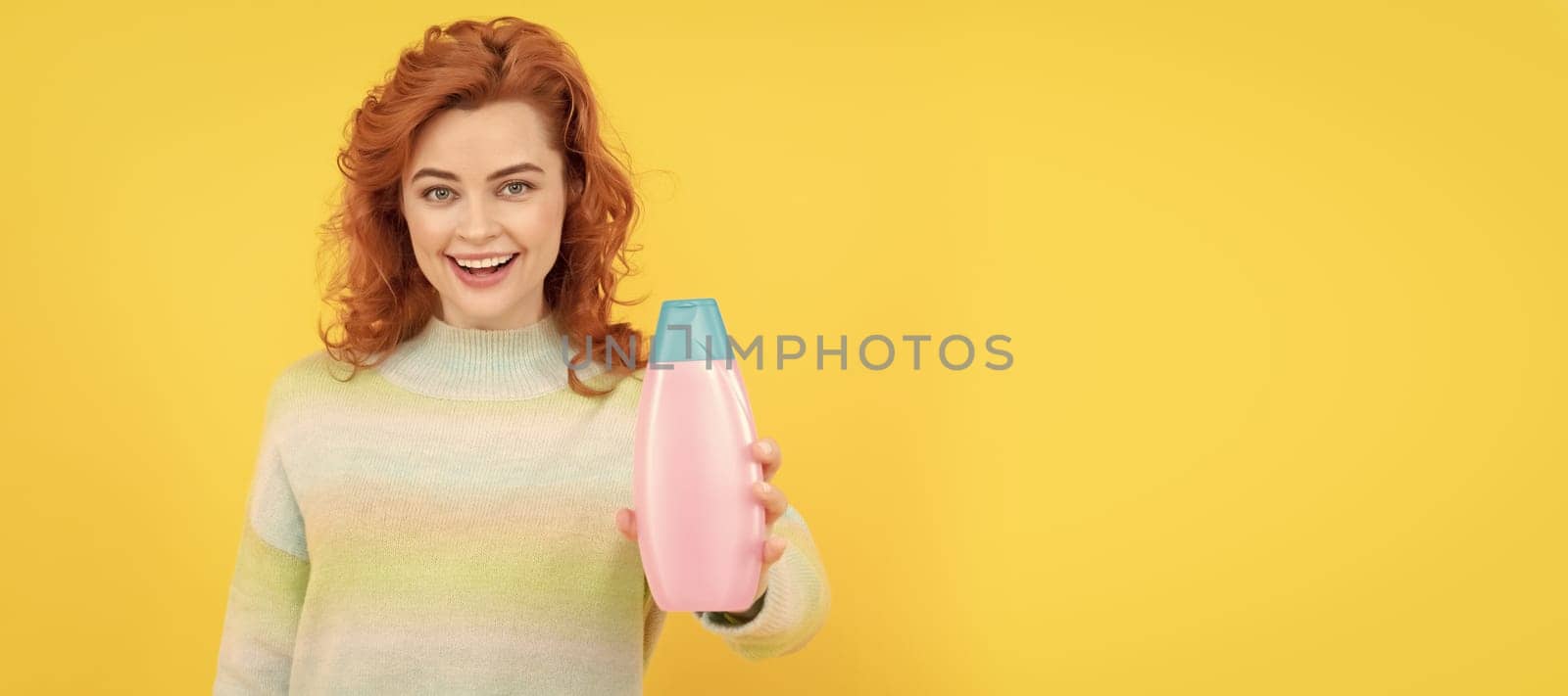 happy redhead woman with curly hair offering shampoo or conditioner, body care. Woman isolated face portrait, banner with copy space