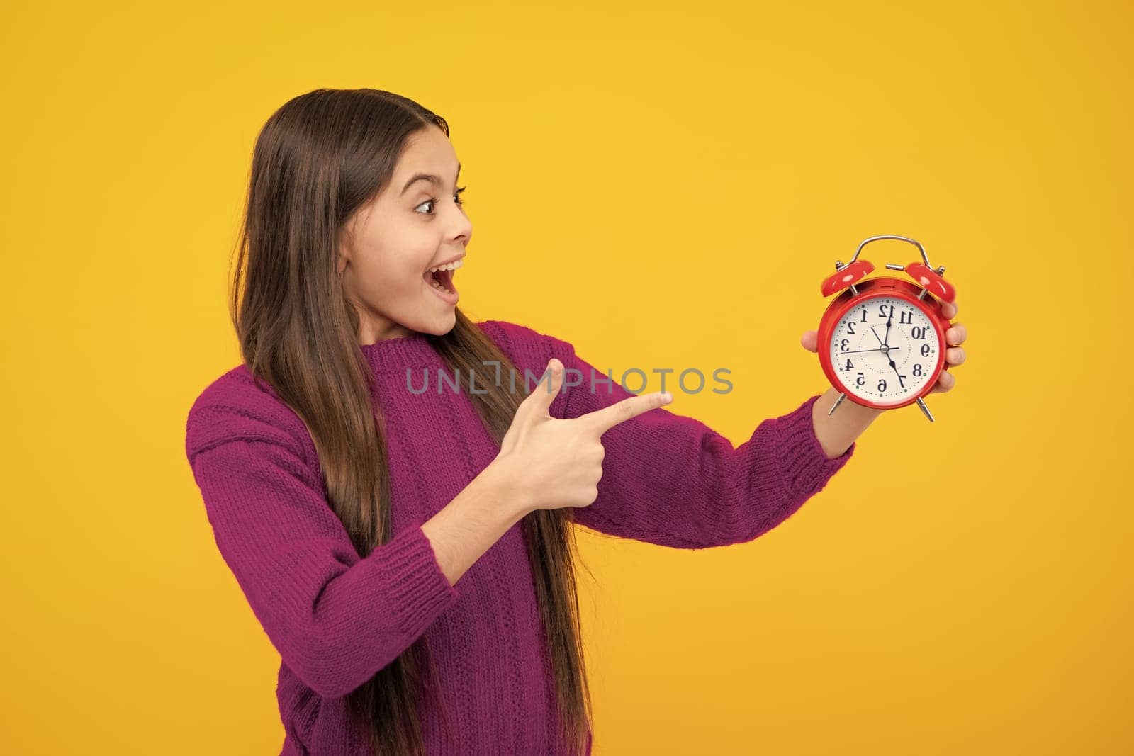 Excited face. Portrait of teenage girl with clock alrm, time and deadline. Studio shot isolated on yellow background. Amazed expression, cheerful and glad