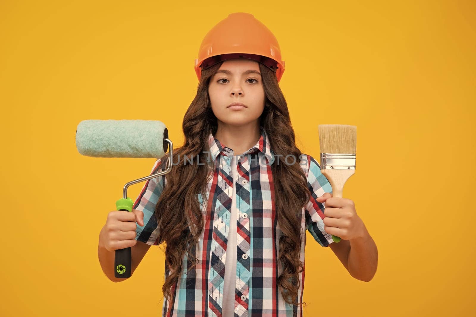 Kids renovation and building concept. Little girl in protective helmet and paint brush for painting walls. by RedFoxStudio