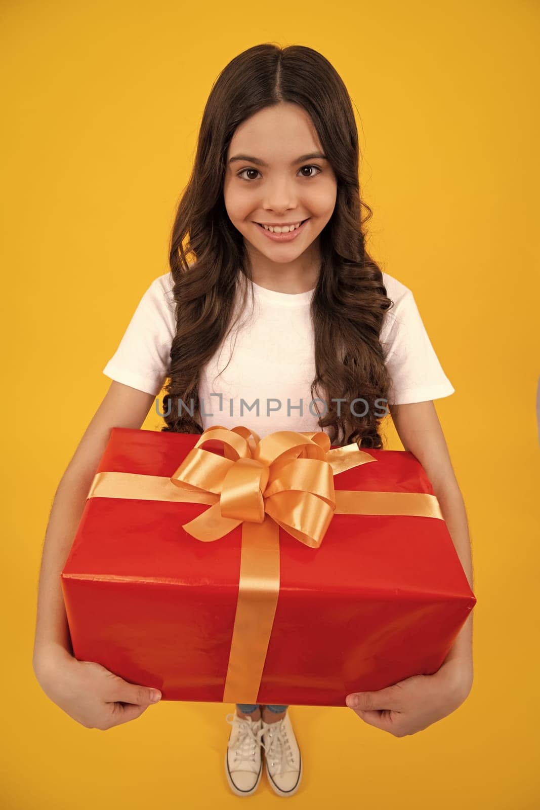 Happy teenager, positive and smiling emotions of teen girl. Teenager child in t shirt holding gift box on yellow isolated background. Gift for kids birthday. Summer holiday