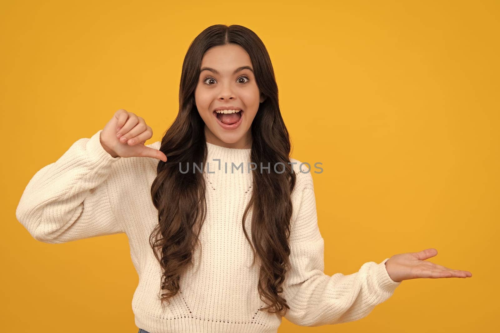 Excited teenager girl. Look at advert. Teenager child points aside shows blank copy space for text promo idea presentation, poses against yellow background. by RedFoxStudio