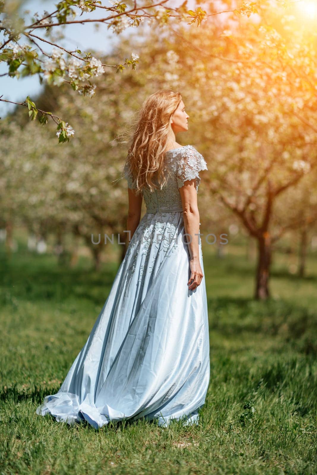 Blond garden. Portrait of a blonde in the park. Happy woman with long blond hair in a blue dress. by Matiunina