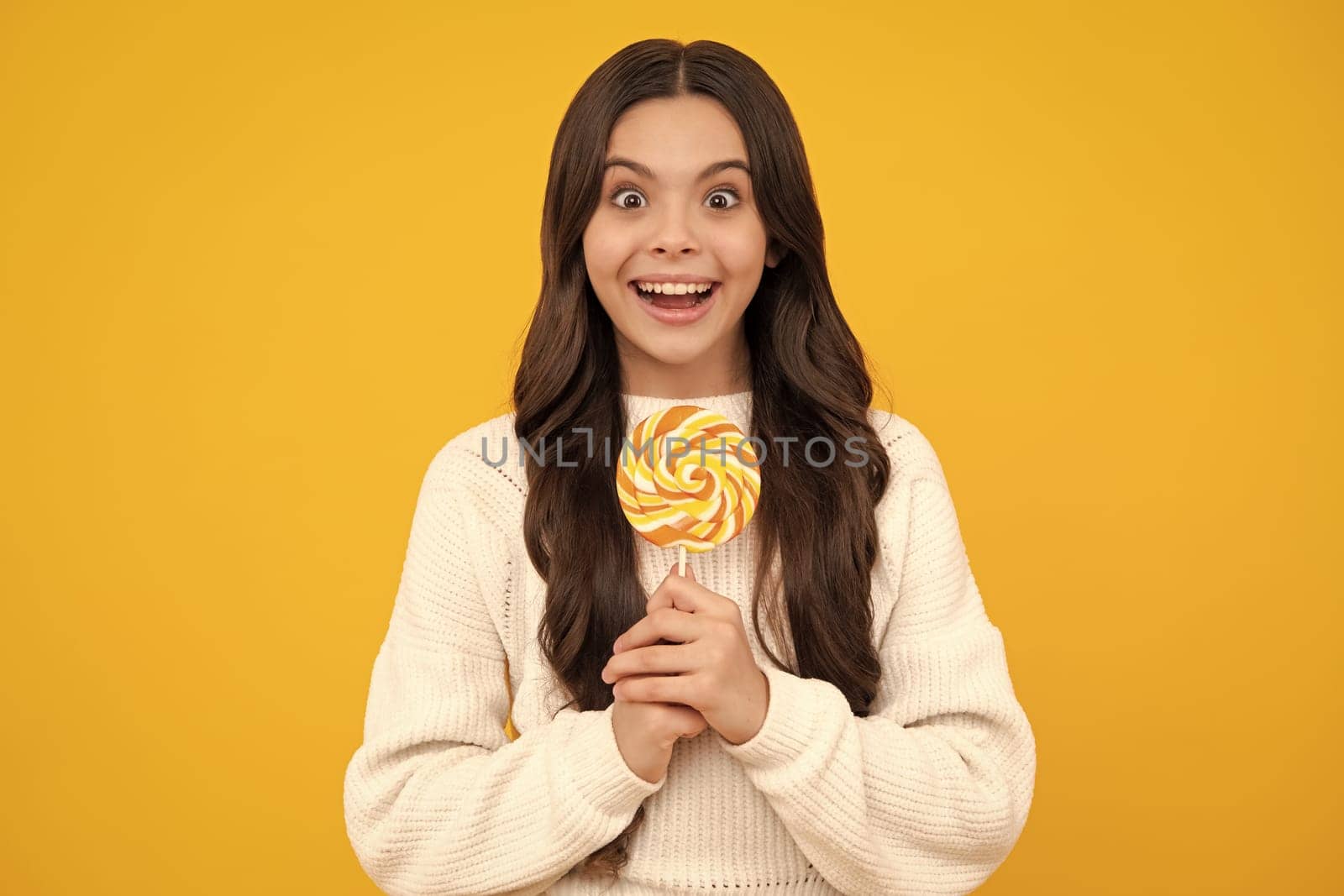 Teen girl hold lollipop caramel on yellow background, candy shop. Teenager with sweets suckers. Happy face, positive and smiling emotions of teenager girl. by RedFoxStudio