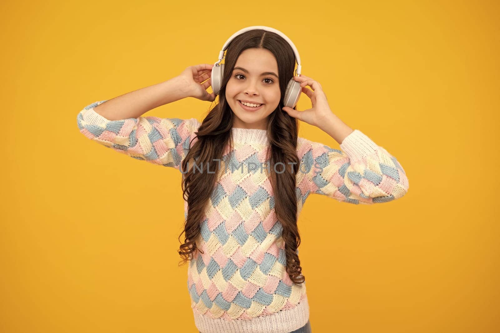 Teen girl in headphones listen to music. Wireless headset device accessory. Child enjoys the music in earphones on yellow background