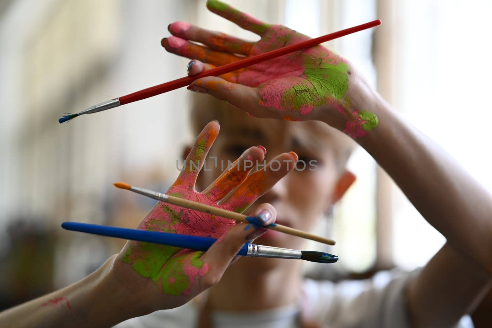 Artist hands soiled with watercolor paints holding brushes and smiling to camera. Art, hobby and leisure activity concept.