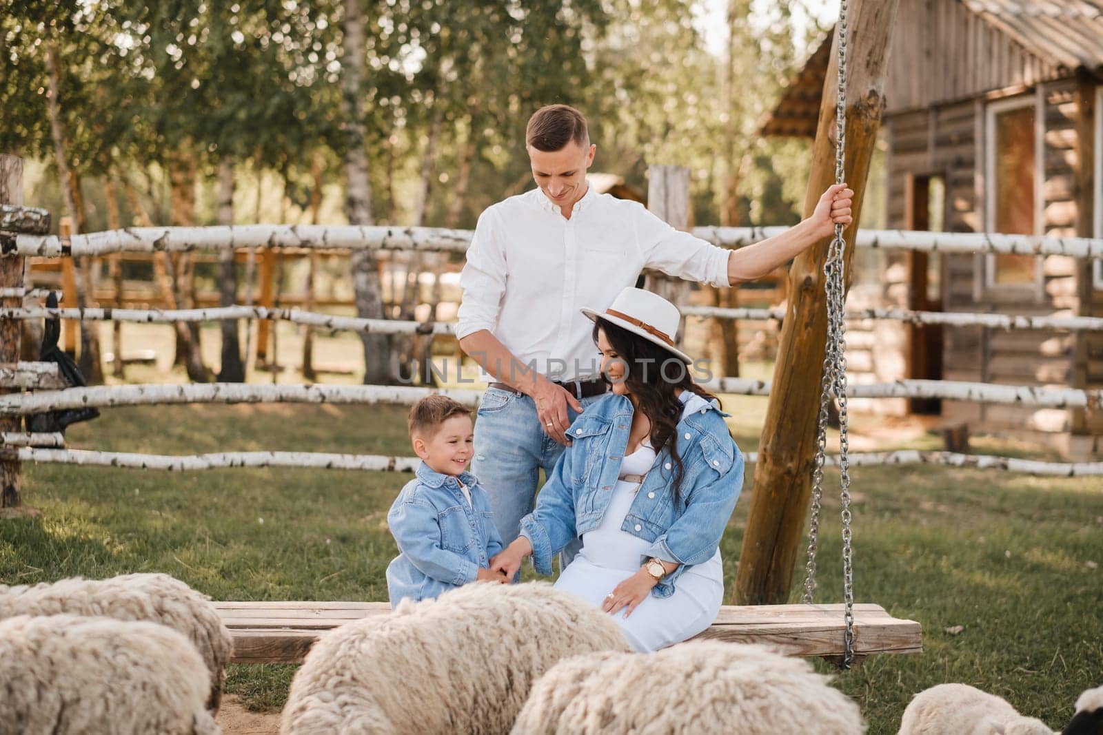 Stylish family in summer on a village farm with sheep.