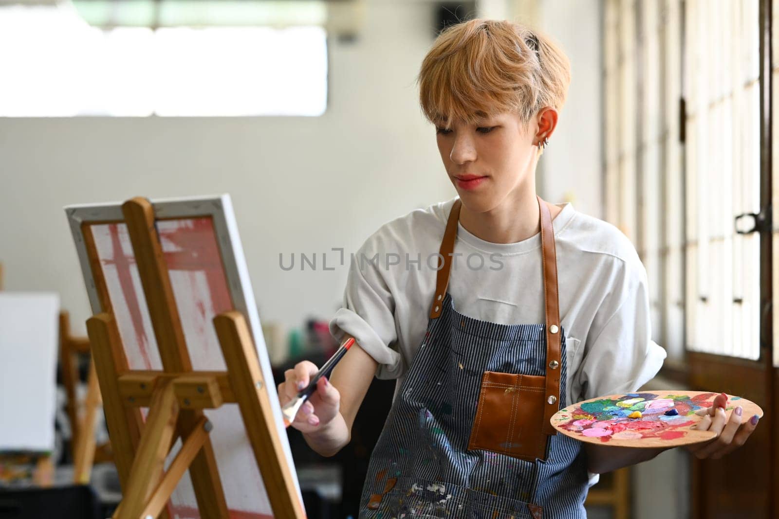 Creative young asian gay man making a new painting on a canvas. Art and education concept.