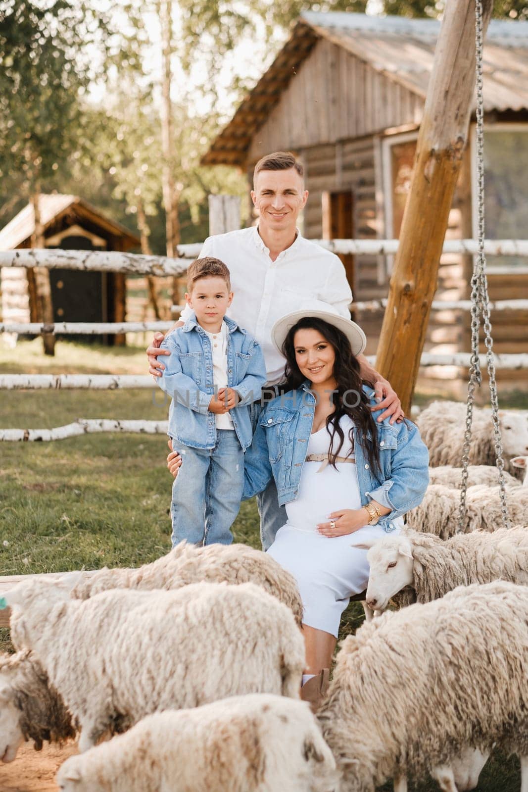 Stylish family in summer on a village farm with sheep.