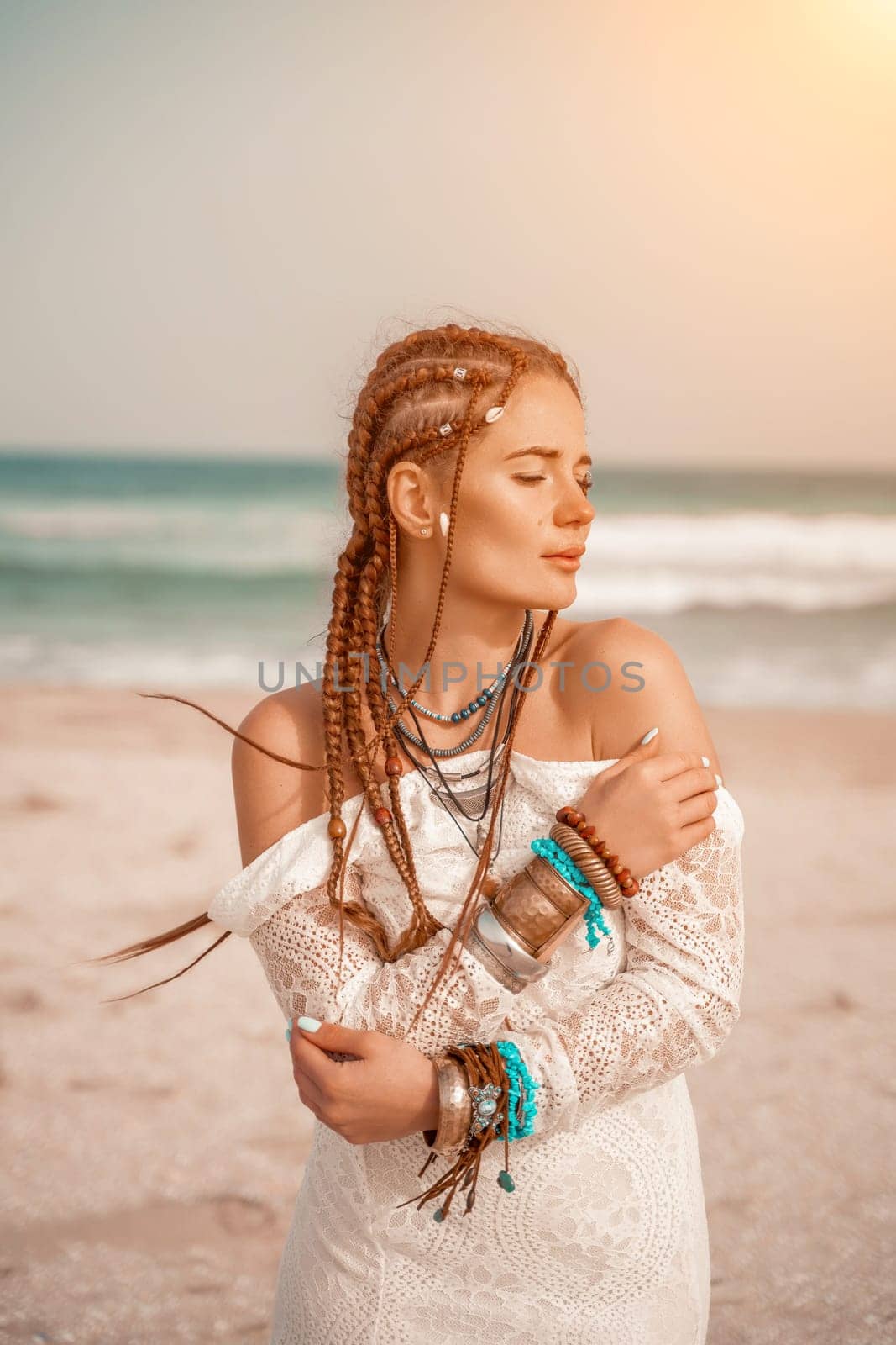 Woman portret sea white dress. Model in boho style in a white long dress and silver jewelry on the beach. Her hair is braided, and there are many bracelets on her arms