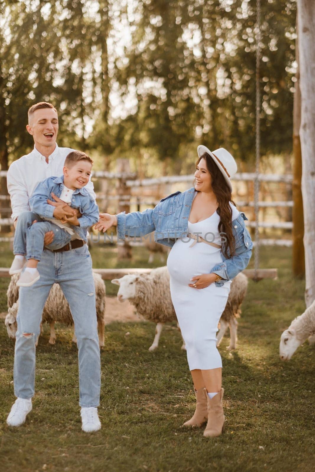 Stylish family in summer on a village farm with sheep.