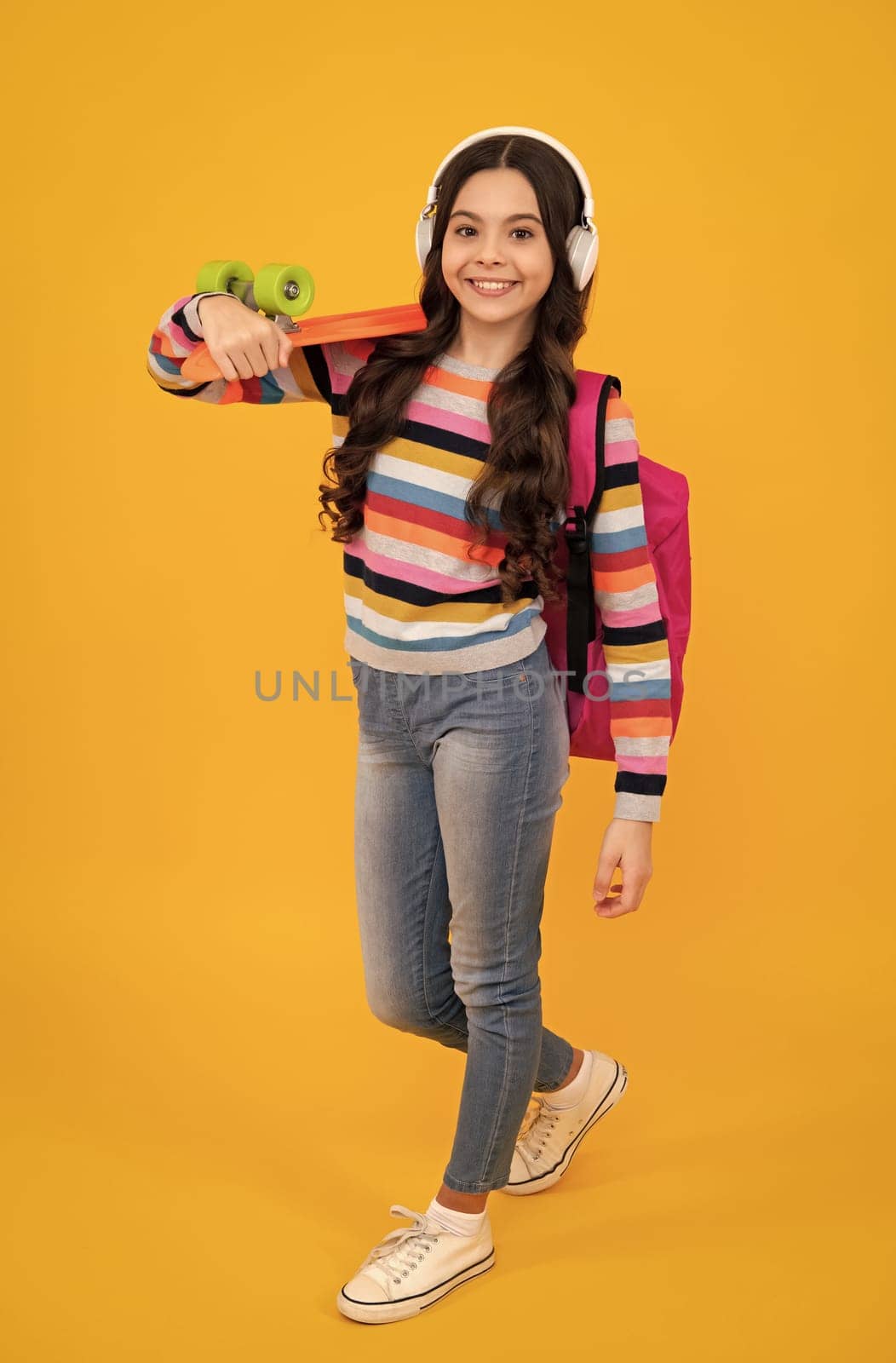 Teen girl 12, 13, 14 years old with skateboard and headphone over studio background. Cool modern teenager in stylish clothes. Teenagers lifestyle, casual youth culture. Happy teenager. by RedFoxStudio