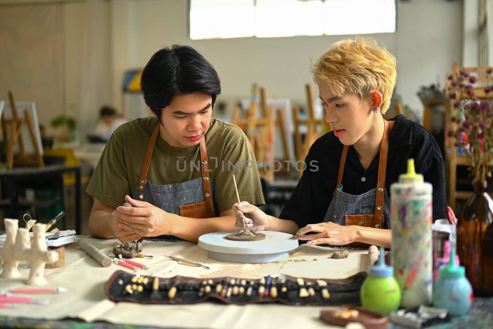 Image of happy gay man couple enjoying creative process, creating handmade ceramics in art class.
