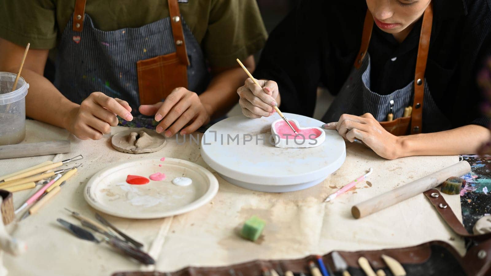 Cropped shot of man decorating clay plate on table at ceramic workshop. Indoors lifestyle activity and hobbies concept by prathanchorruangsak