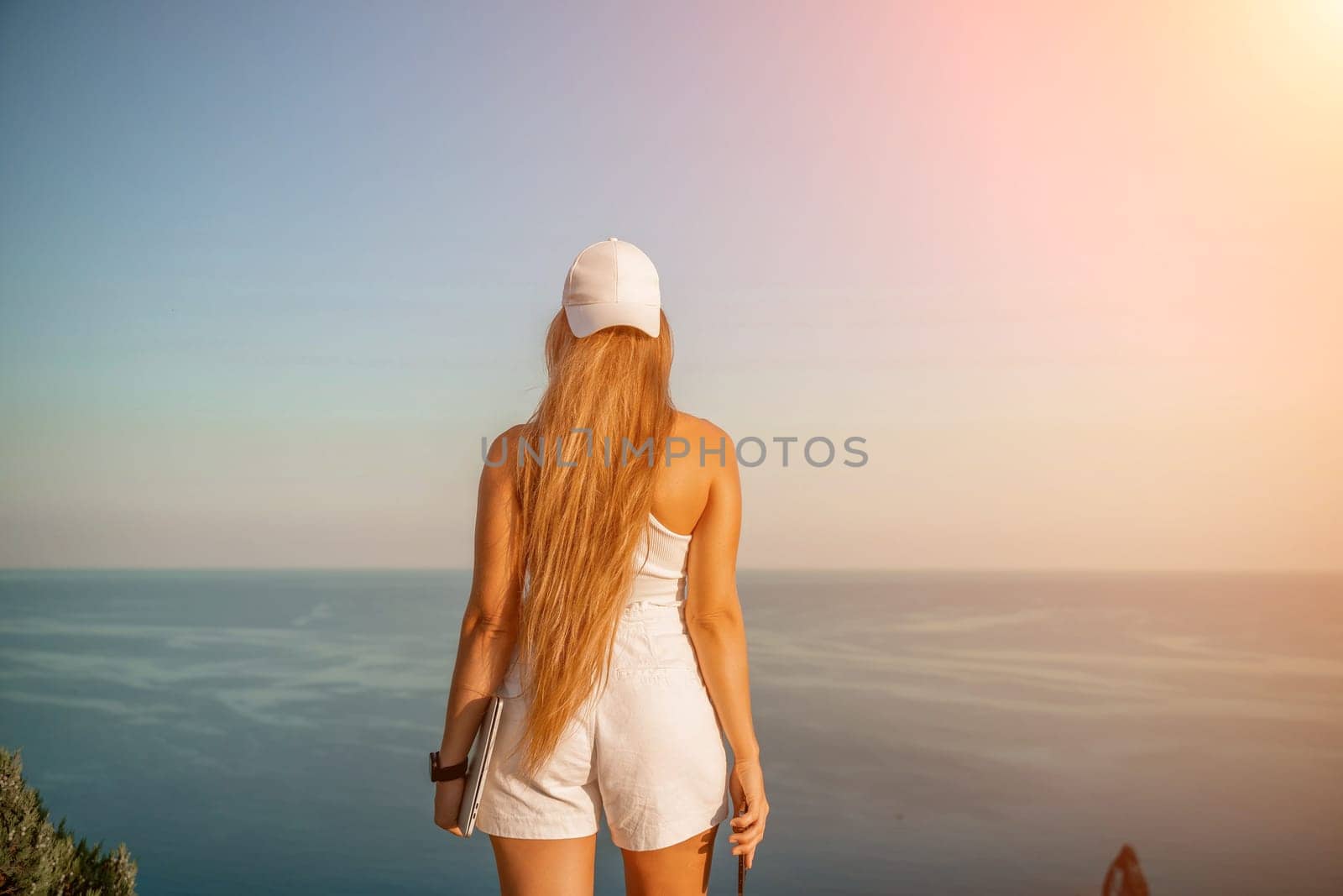 A female tourist stands by the sea wearing a white cap and T-shirt, looking happy and relaxed