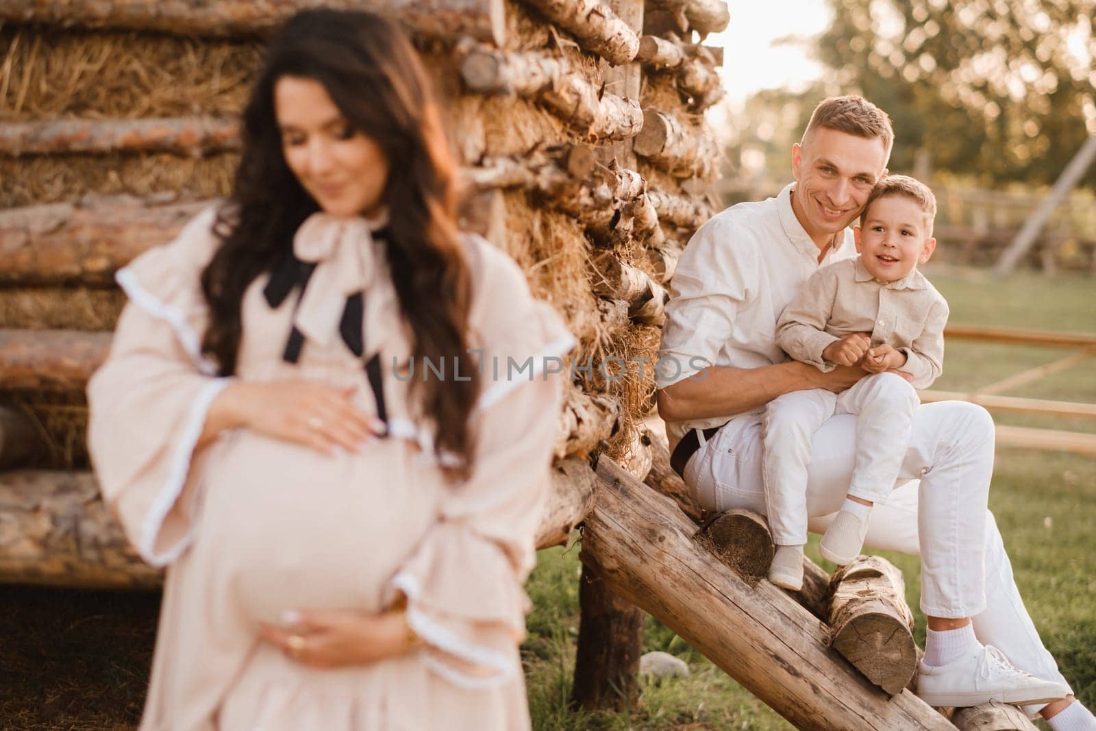 A stylish family in the countryside at sunset. A pregnant woman with her husband and son in nature.