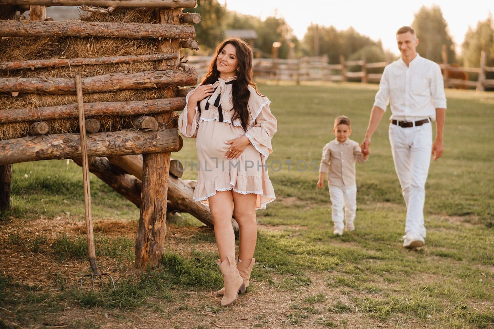 A stylish family in the countryside at sunset. A pregnant woman with her husband and son in nature.