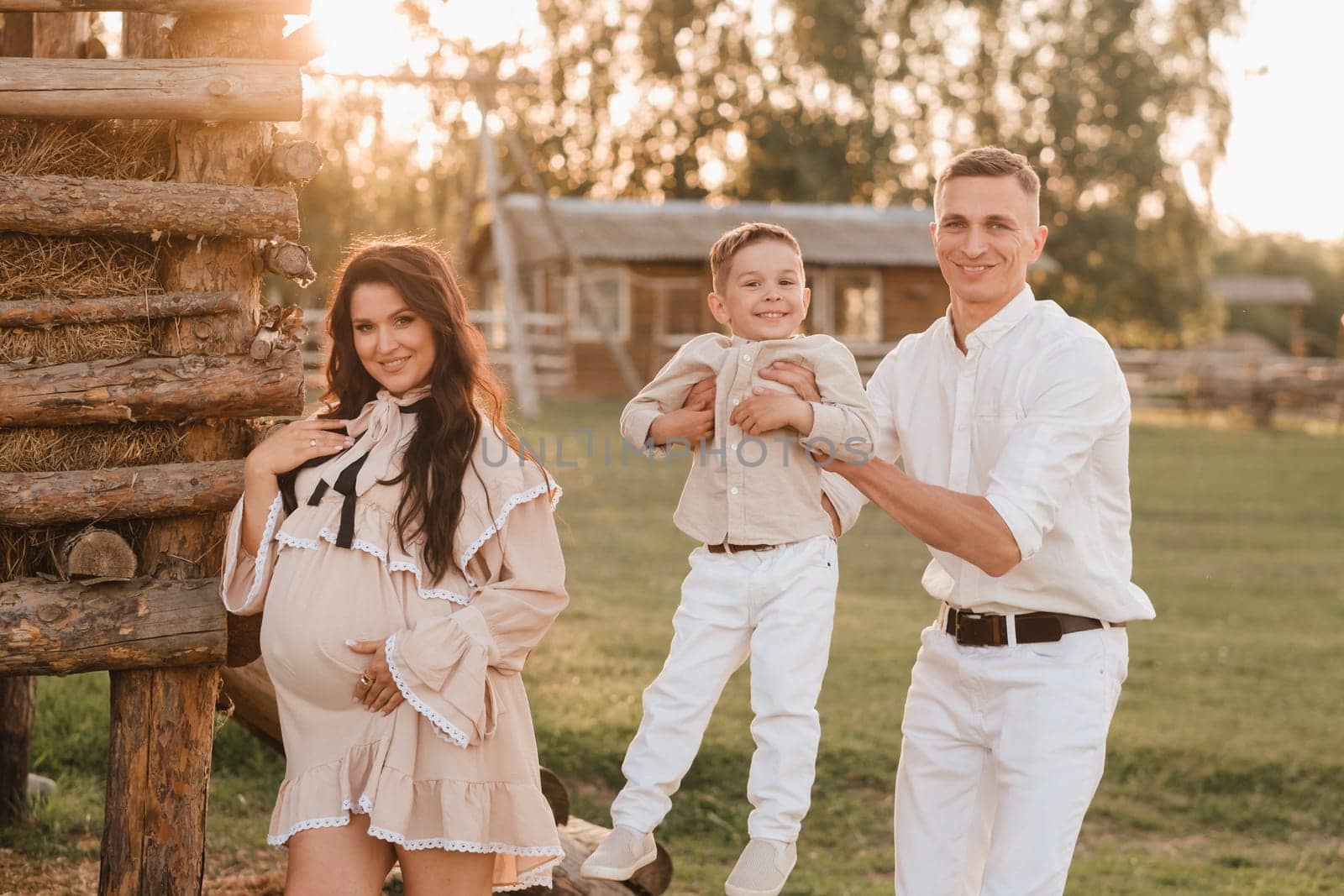 A stylish family in the countryside at sunset. A pregnant woman with her husband and son in nature.