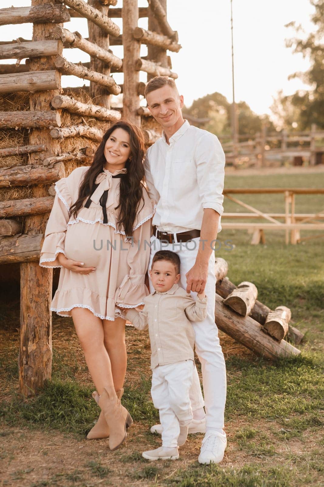 A stylish family in the countryside at sunset. A pregnant woman with her husband and son in nature.