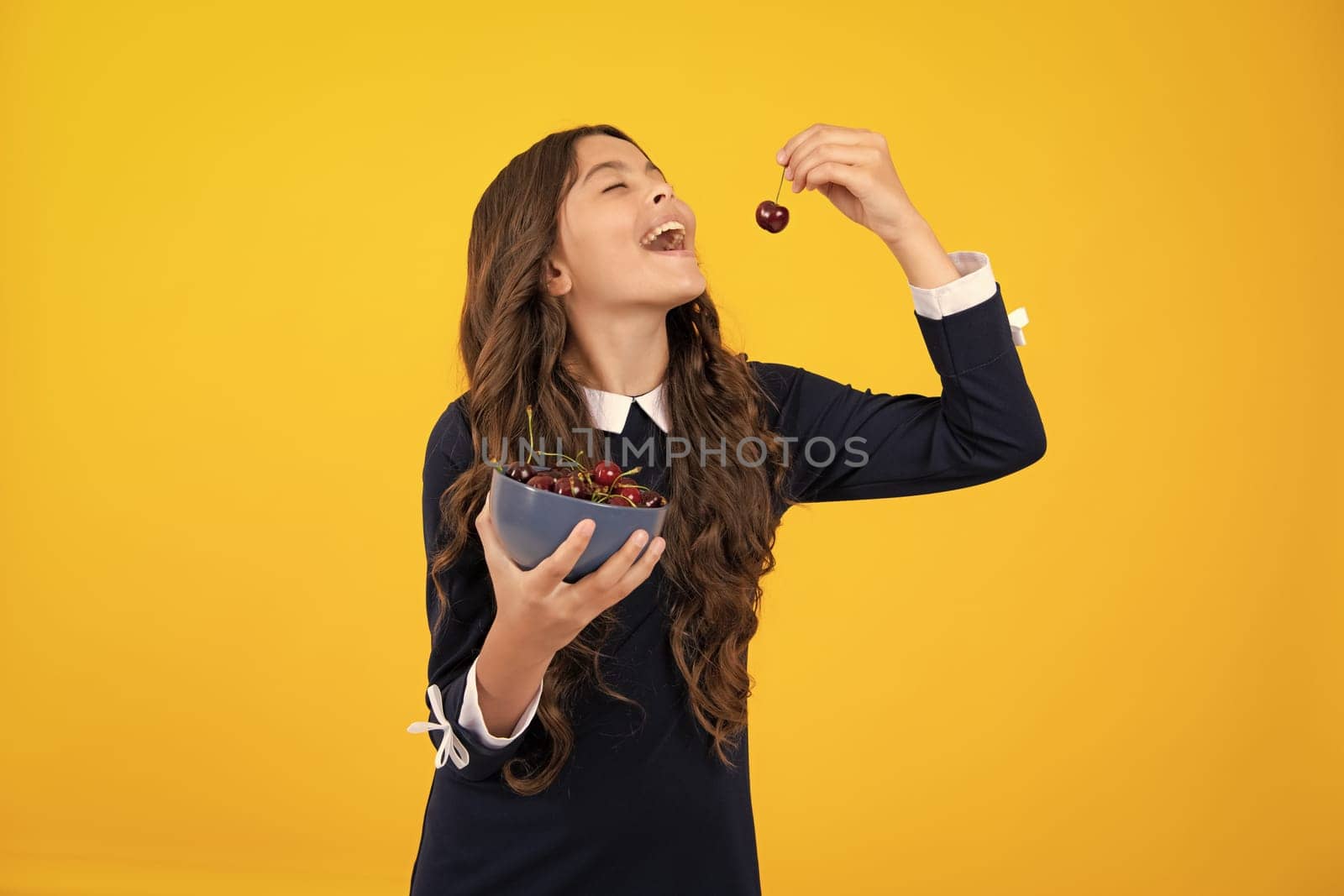 Teenager child girl eating cherries, isolated on yellow background. Summer berries, kids healthy cherry fruits