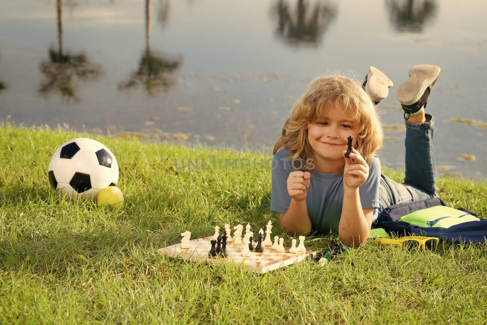 Concentrated kid developing chess strategy, playing board game in backyard, laying on grass