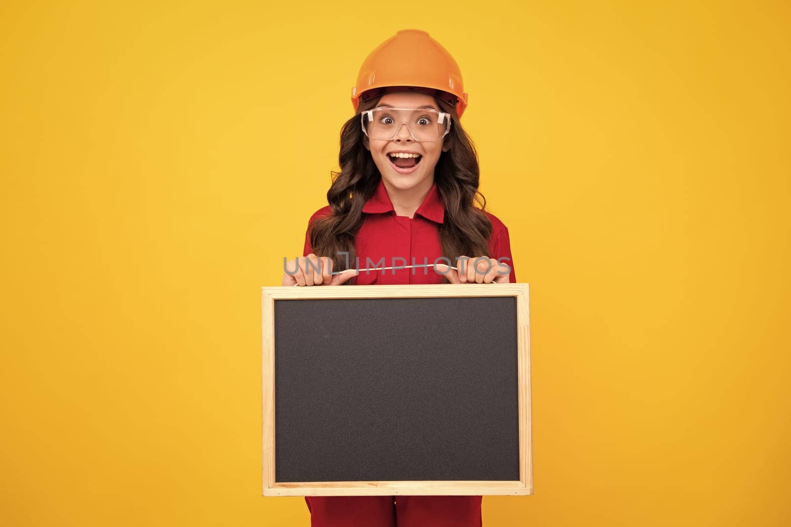 Excited teenager girl. Child builder in helmet. Teenage girl painter with painting brush tool or paint roller. Child on repairing work isolated on yellow background. Kids renovation concept