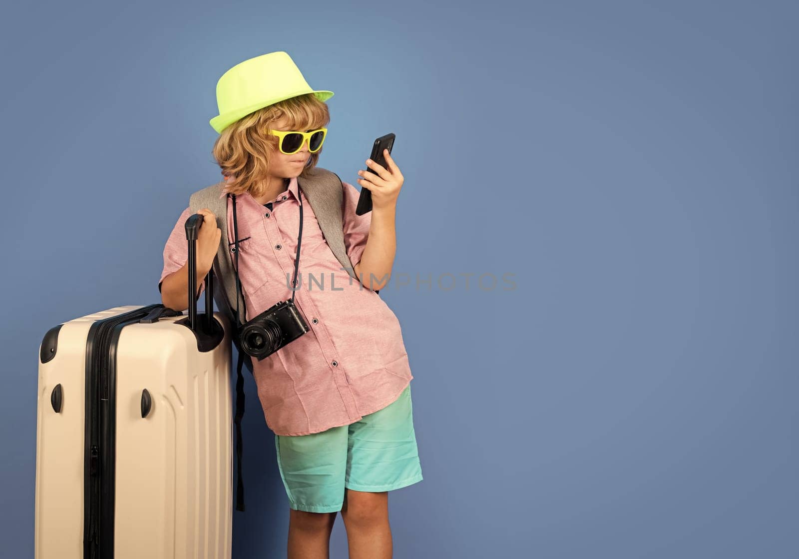 Kids travel. Happy child boy in travel hat with suitcases isolated on studio backgraund. Travel lifestyle and dreams of travel. by RedFoxStudio