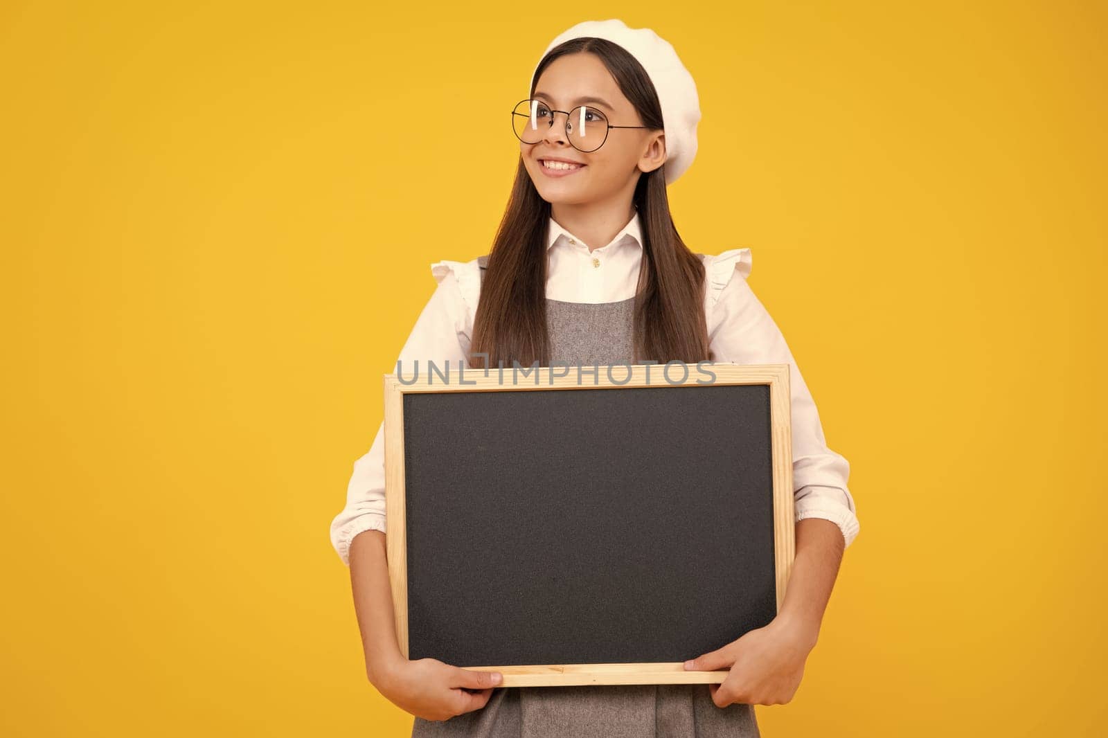 Teenager child holding blank chalkboard for message Isolated on a yellow background. Empty text blackboard, copy space mock up