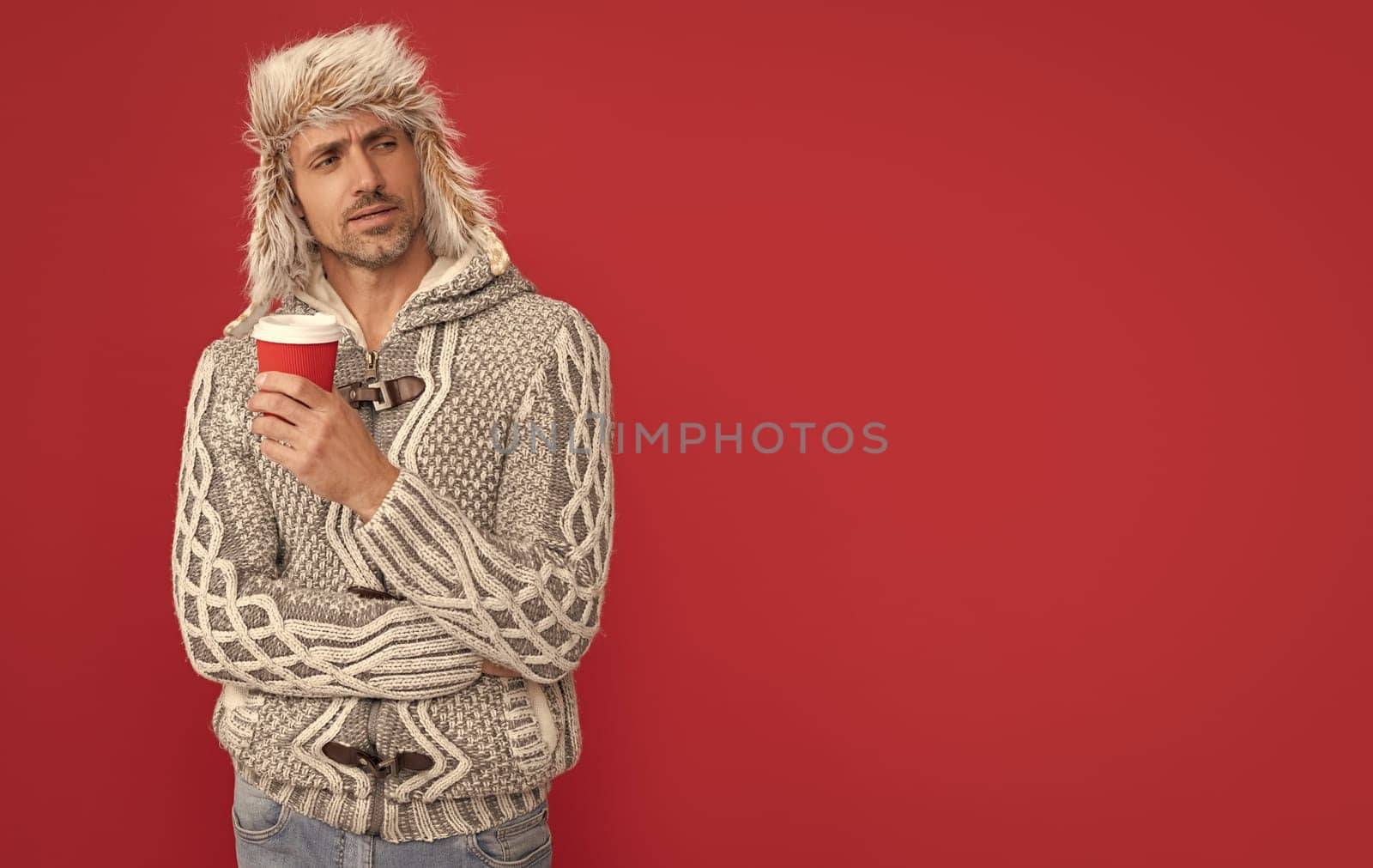 morning coffee in take away cup. serious grizzled guy in sweater and hat on red background. by RedFoxStudio