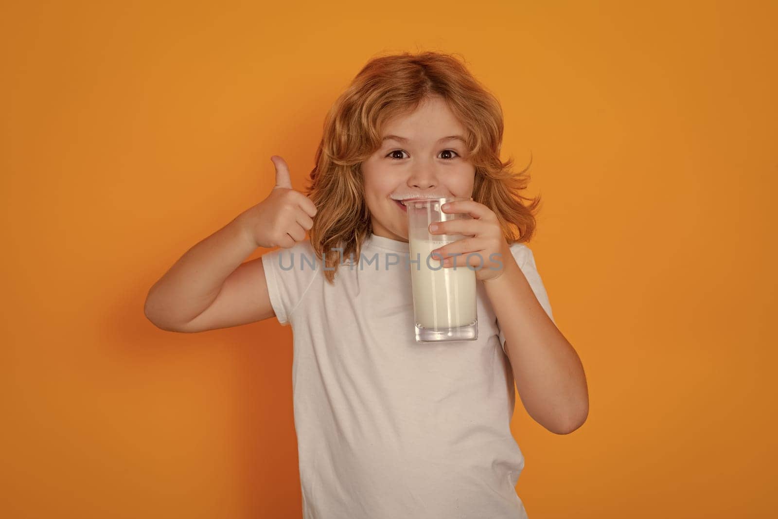 Dairy milk. Child with a glass of milk. Cute boy in white shirt holding glass of milk on yellow isolated studio background. Portrait of funny kid with milk mustache